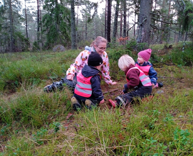 Barn leker ute i skogen med förskolelärare